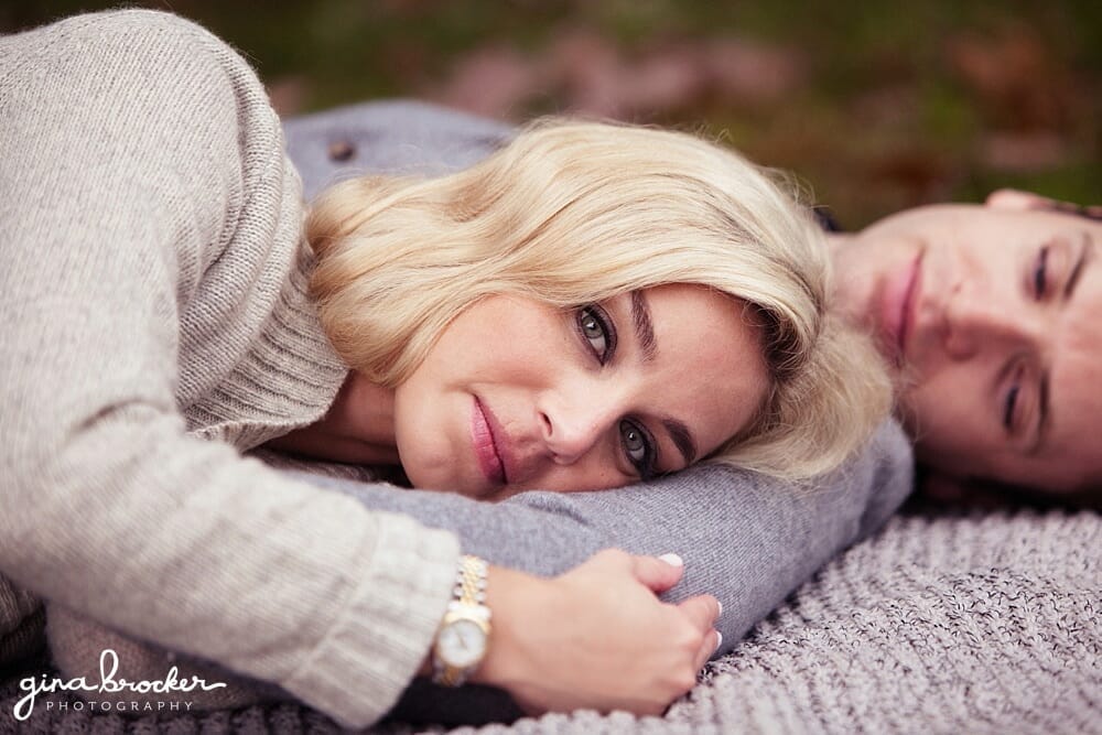 A man looks at his bride to be as they lay a blanket during their cozy fall new england engagement session