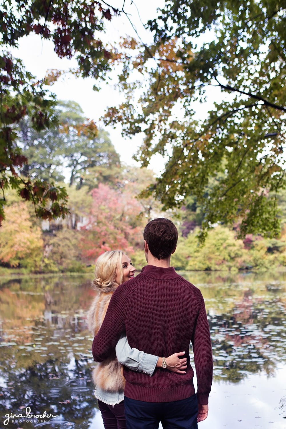 A couple cuddle as the look out onto the water during their fall engagement session in new england