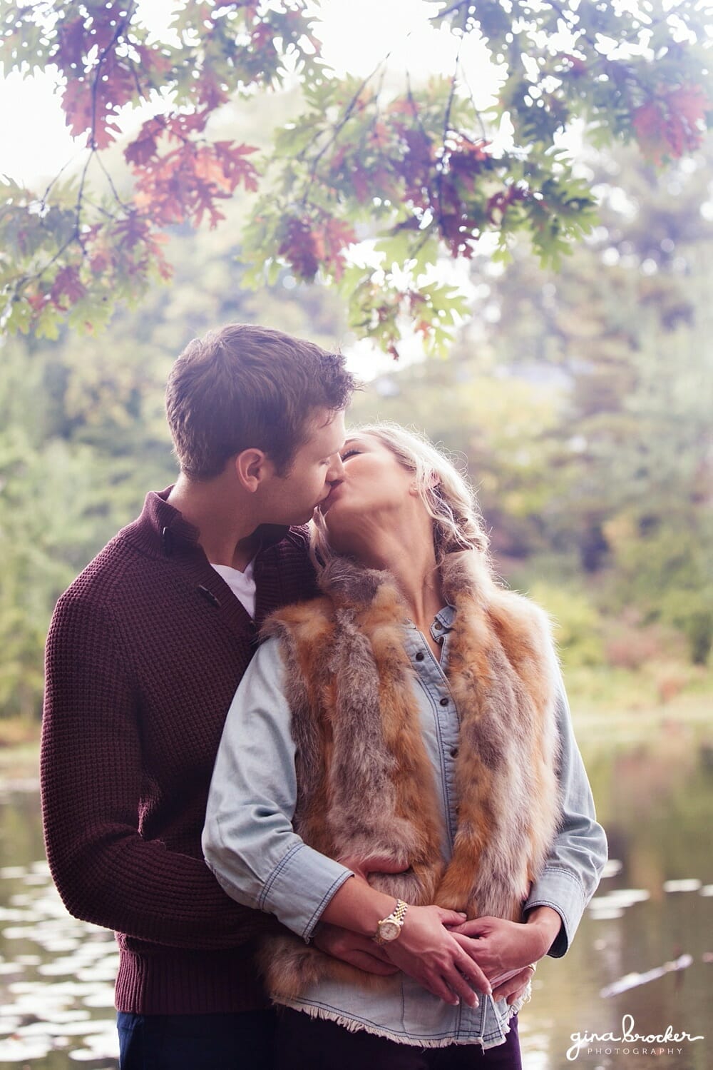 Couple kiss by the charles river during their woodsy engagement session in boston