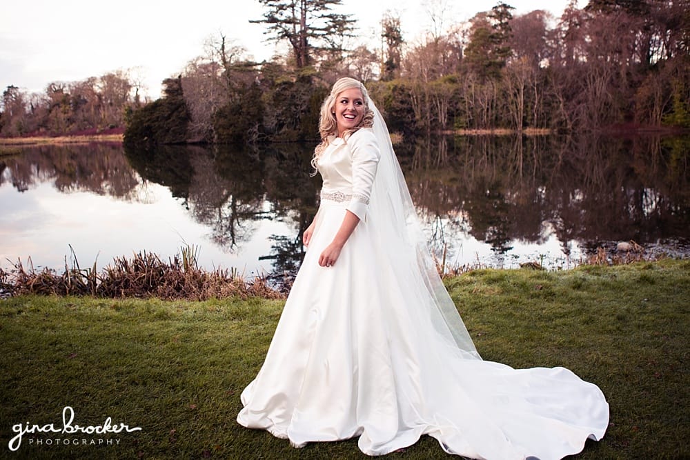 Classic winter wedding bride looks back at husband in front of lake