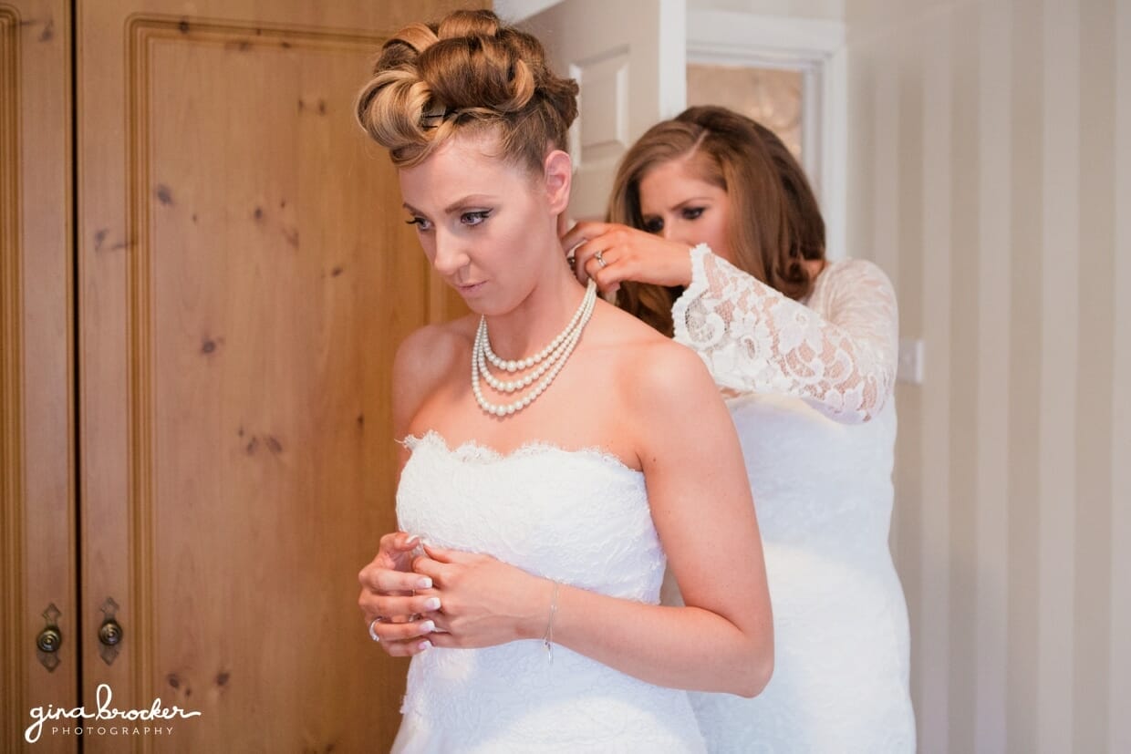 A bridesmaids puts a pearl necklace on the bride before her wedding