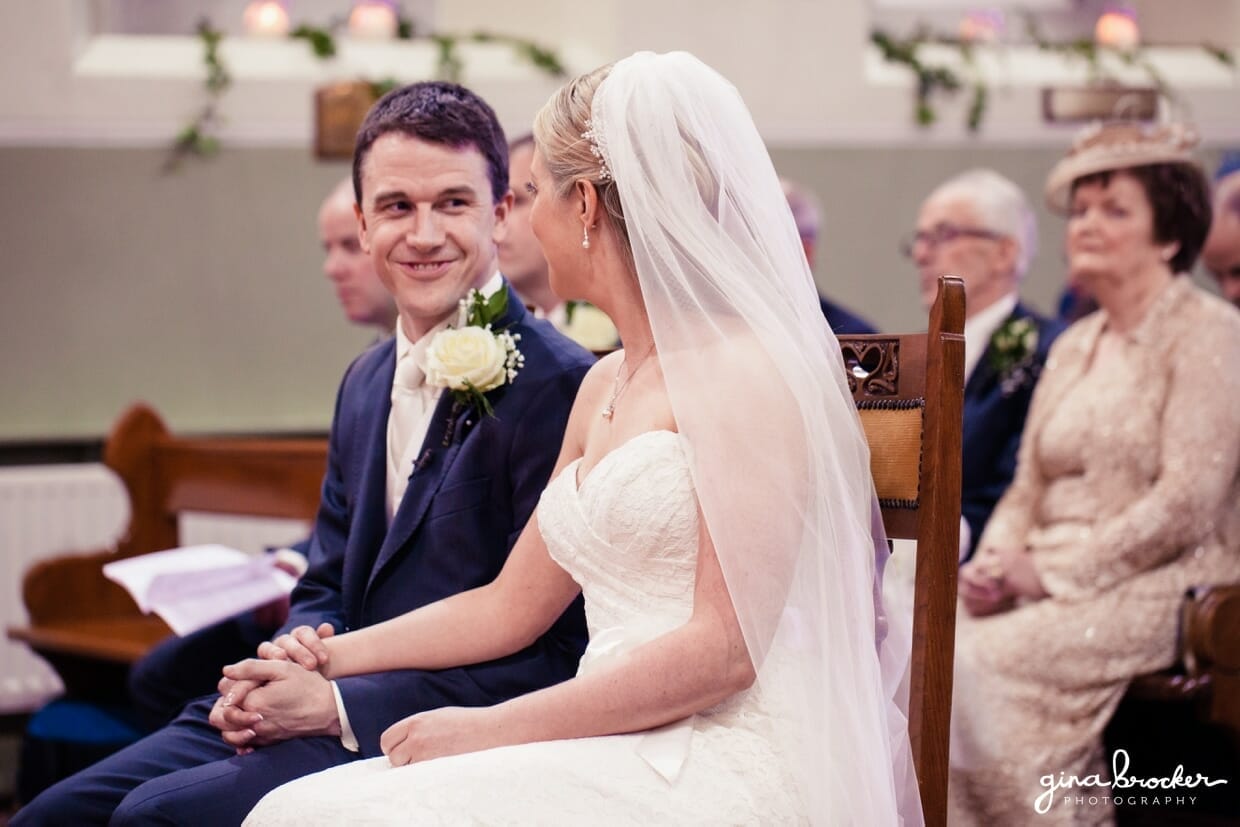 The groom looks at his bride during their classic vintage wedding ceremony in a small and quaint church