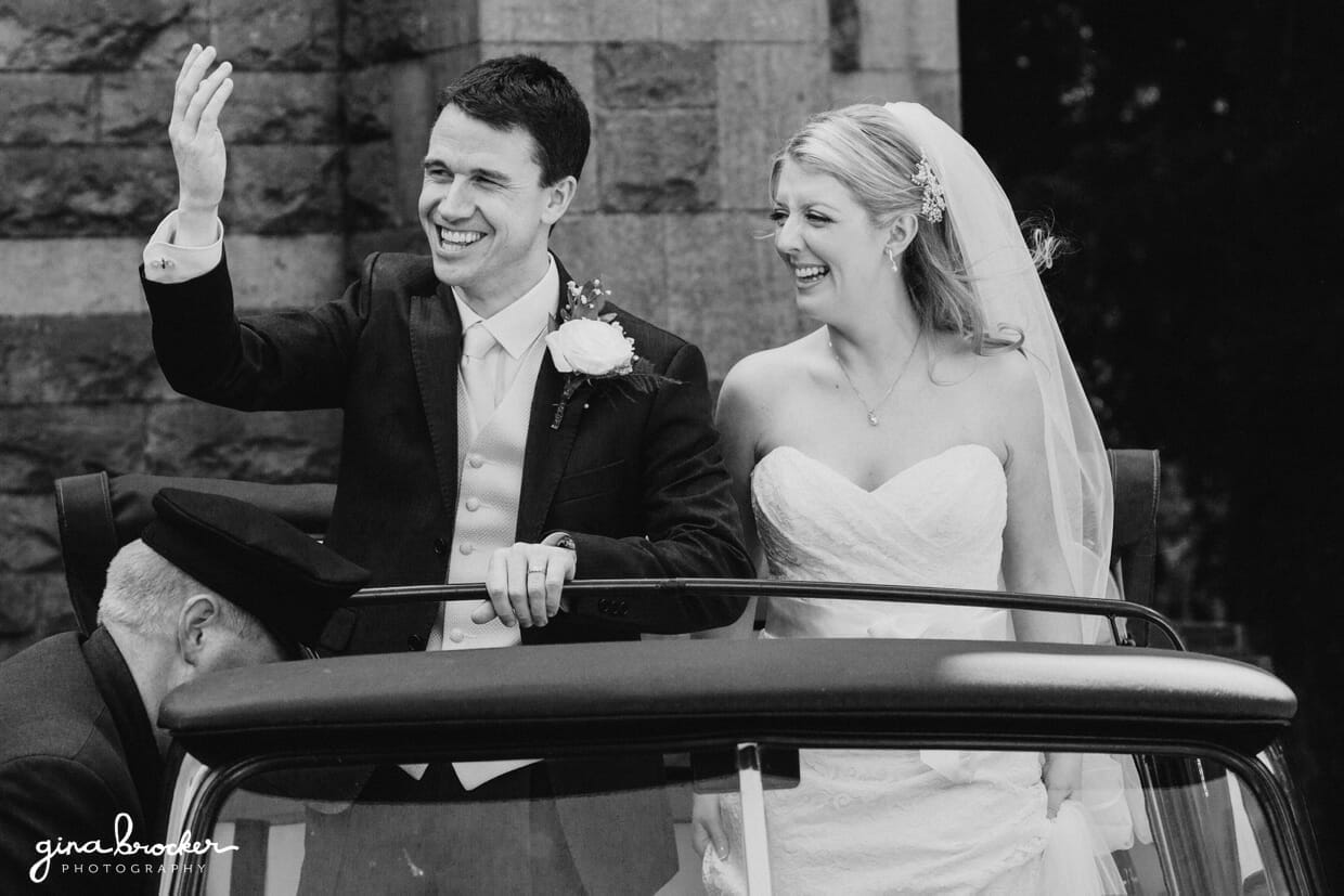 The bride and groom wave to their guests as they leave the in their classic vintage wedding car