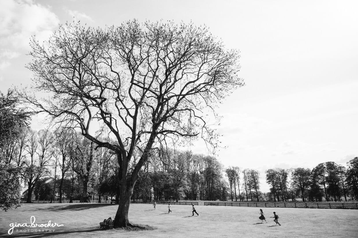 The kids play under a big tree during an outdoor cocktail hour of a classic vintage wedding