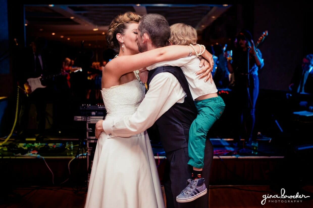 43.first.dance.with.son The bride and groom hug and kiss while they dance with their son during their fun and retro wedding