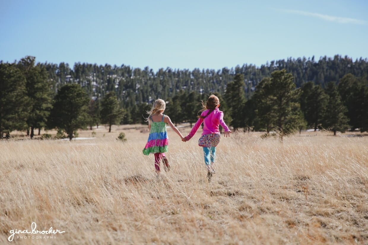 04.sisters.walking.in.field Two sisters hold hands and walk in a field during their lifestyle photography session