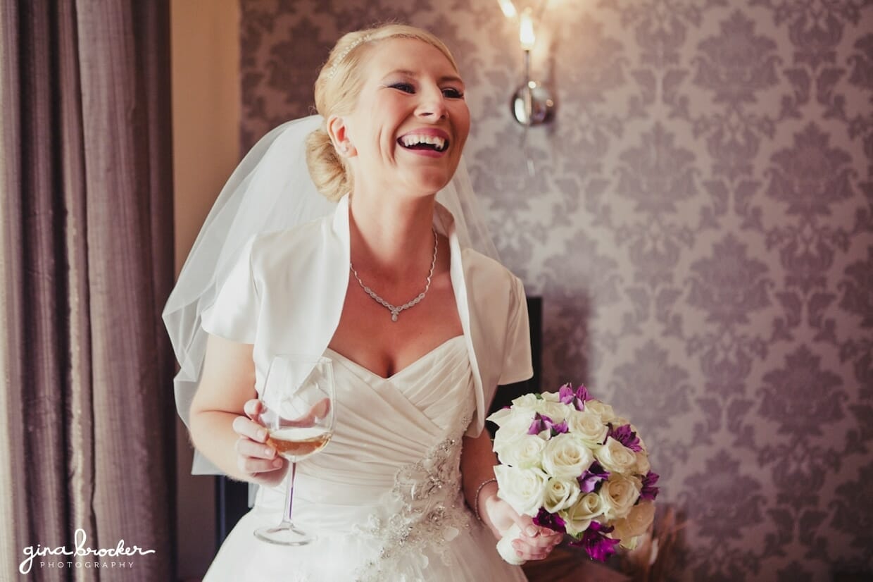 A bride has a glass of champagne and laughs before leaving for her wedding ceremony