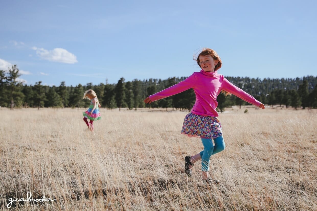 Two young girls dance in a field during their lifestyle photography session