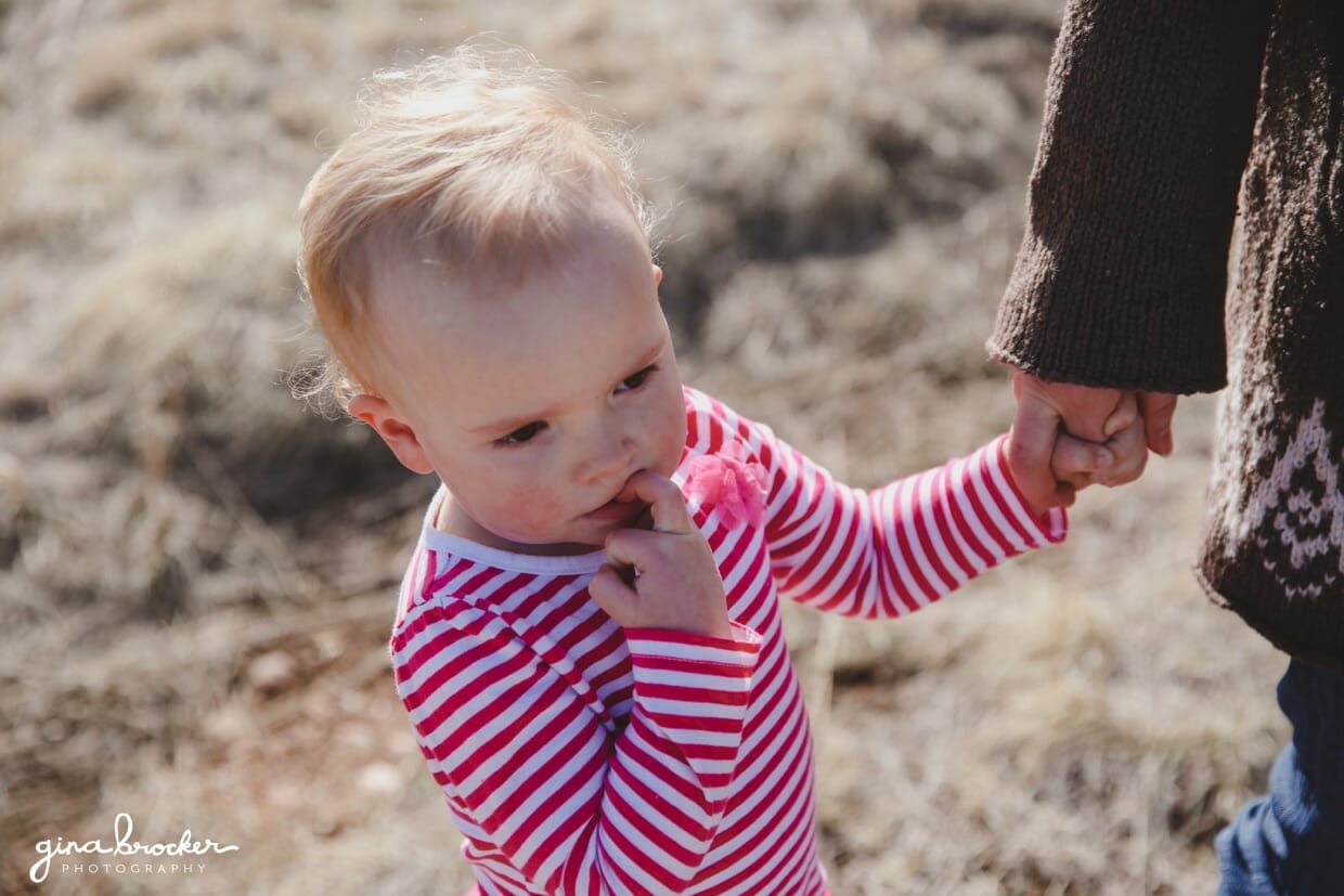 A toddler holds her sisters hand while walking by the mountains