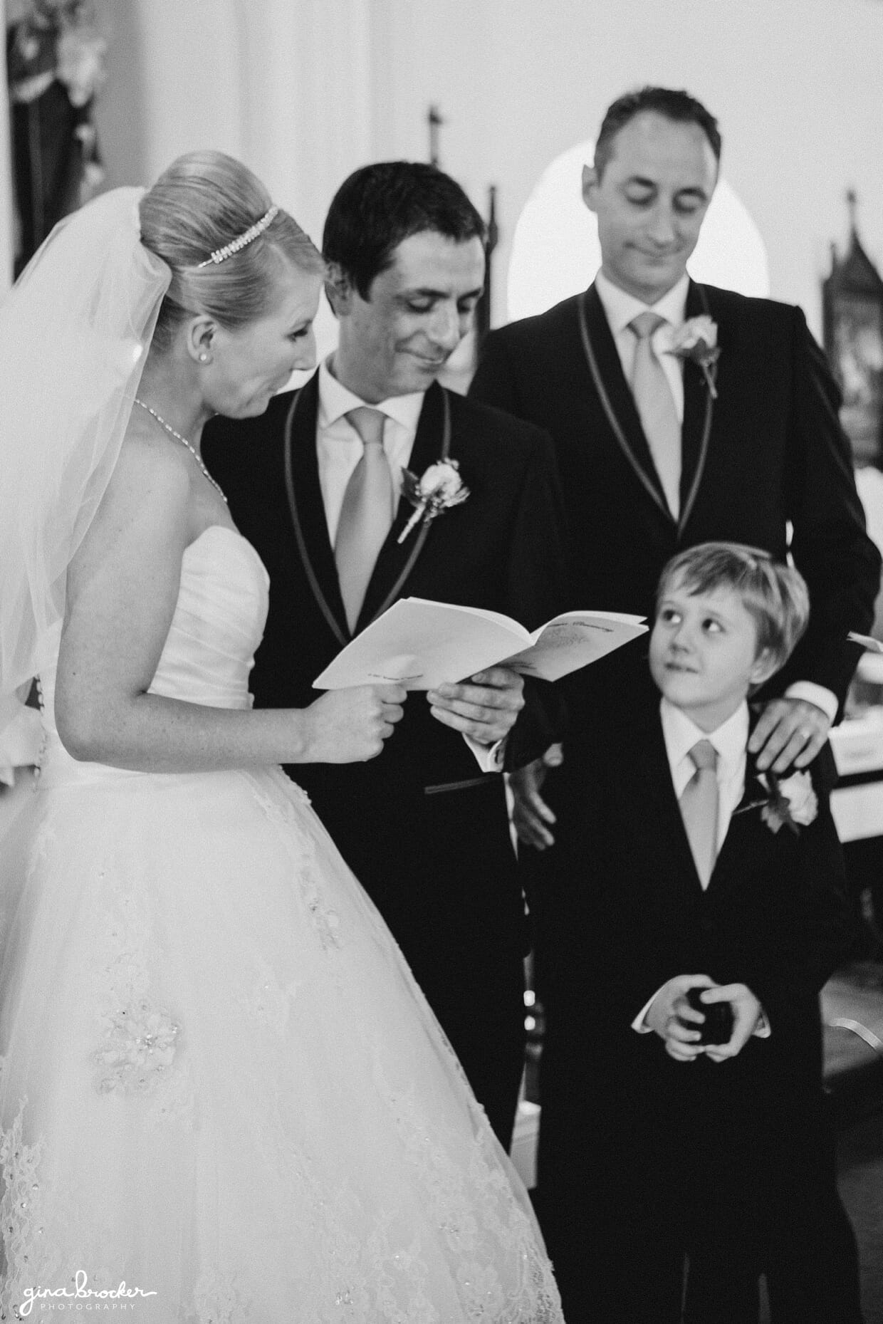 The ring bearer looks up at the bride and groom as they say their wedding vows during their small church wedding ceremony