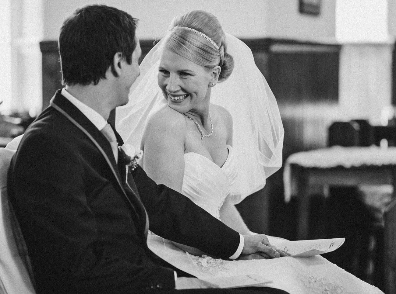 The bride smiles at her new husband as they sit together during their intimate church wedding