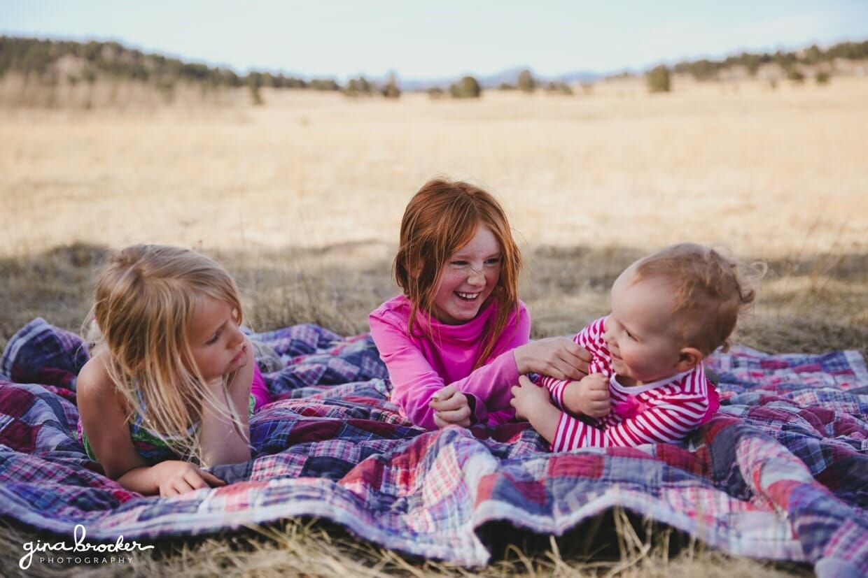 Little girls lay on a blanket outside and laugh during their natural kids photo shoot