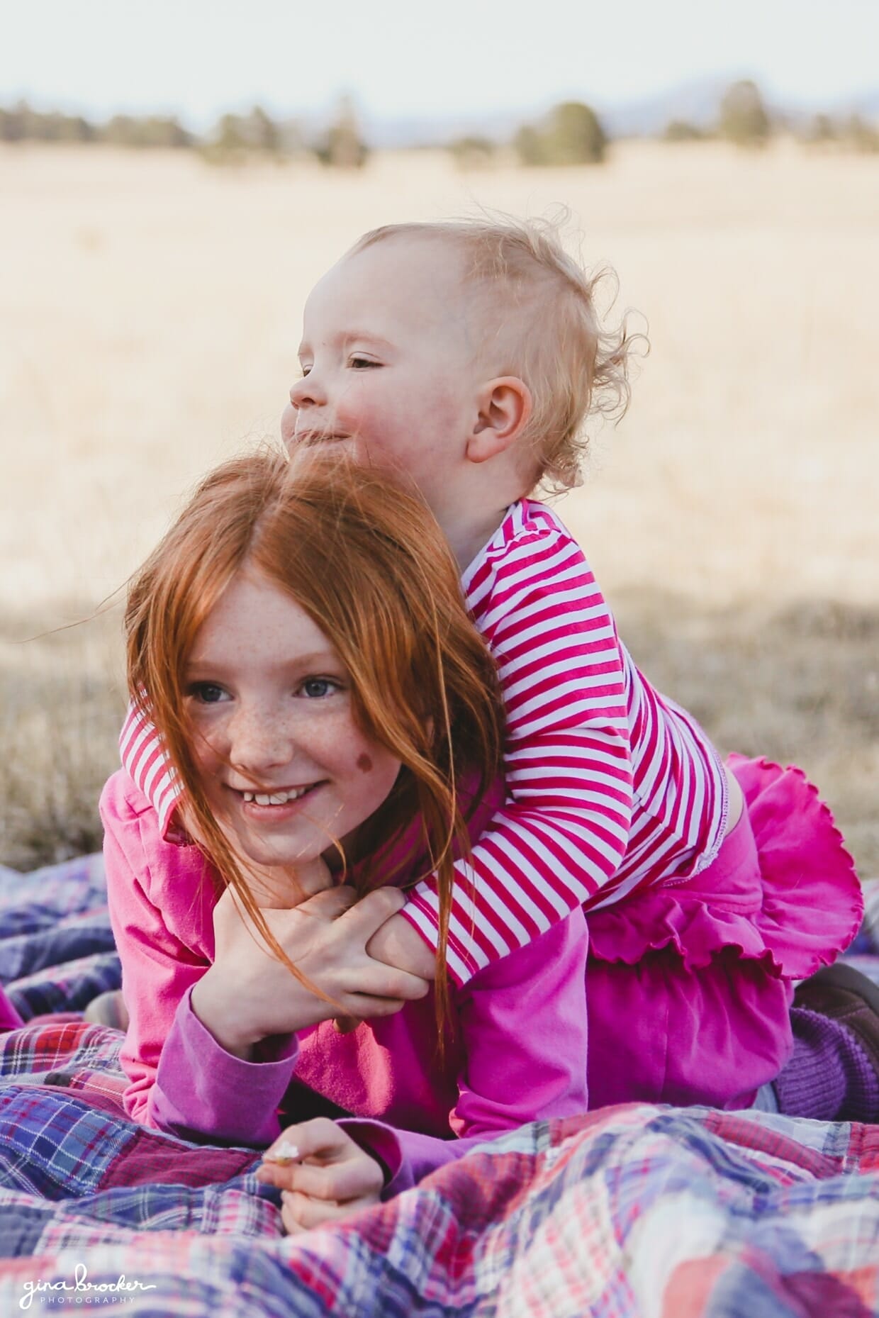 A toddler sits on her sisters back during a fun photo session in a field