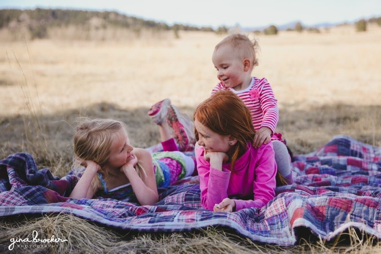 Three girls play on a blanket during their fun and natural outdoor family photo session