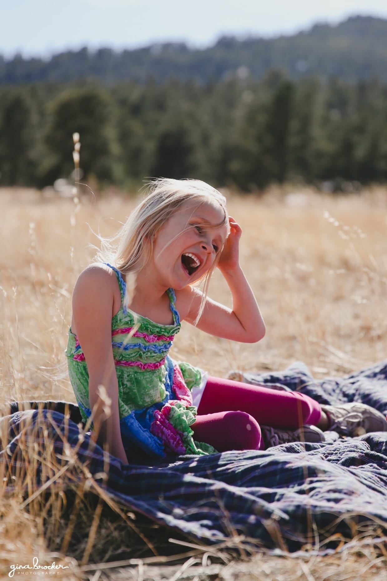 A portrait of a young girl laughing on a blanket during an outdoor family photo session