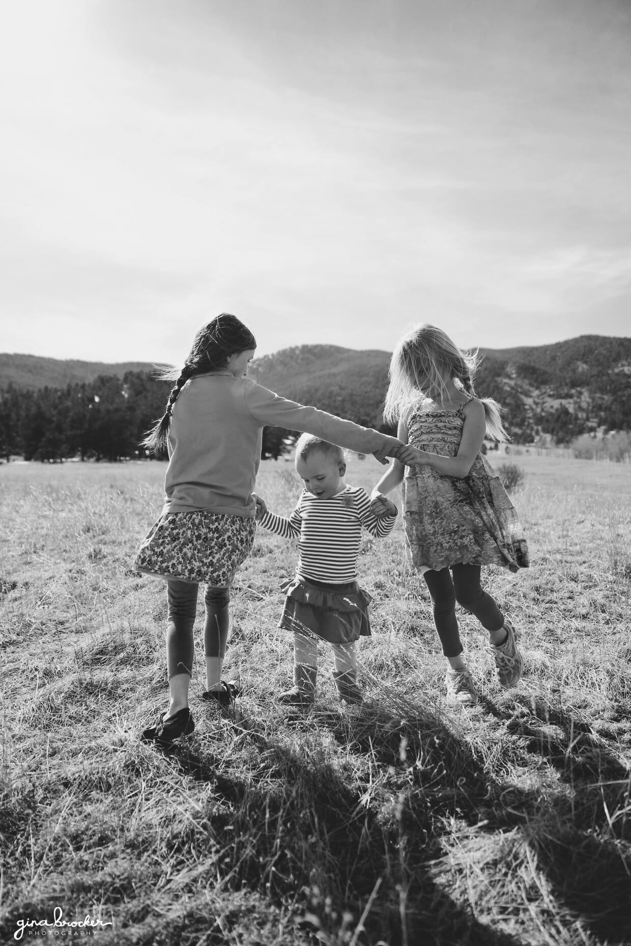 Three sisters play in a field during a natural and candid family photo session