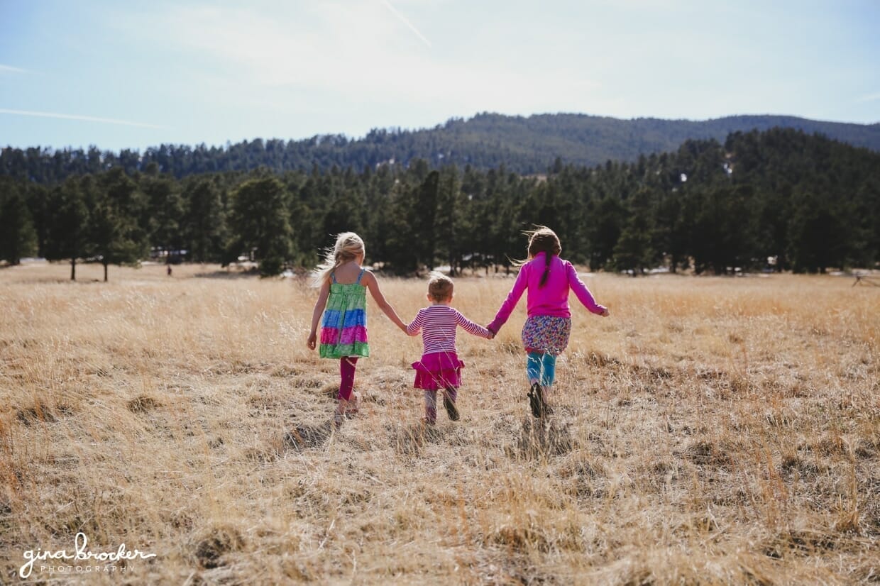 Three sisters hold hands and walk through a field during a beautiful lifestyle photography shoot
