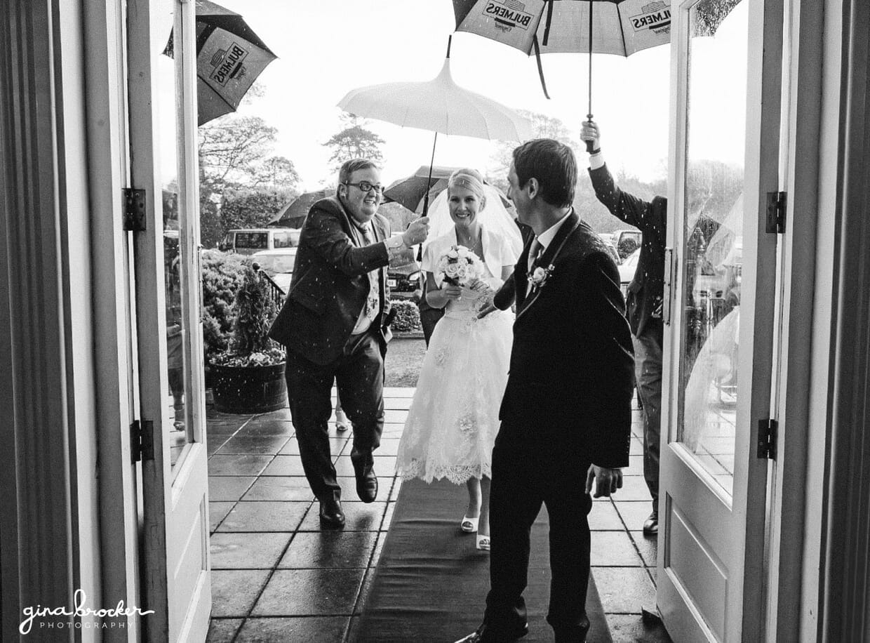 39.bride.and.groom.walk.in.rain The bride and groom run into their venue with umbrellas as it starts to rain during their retro wedding