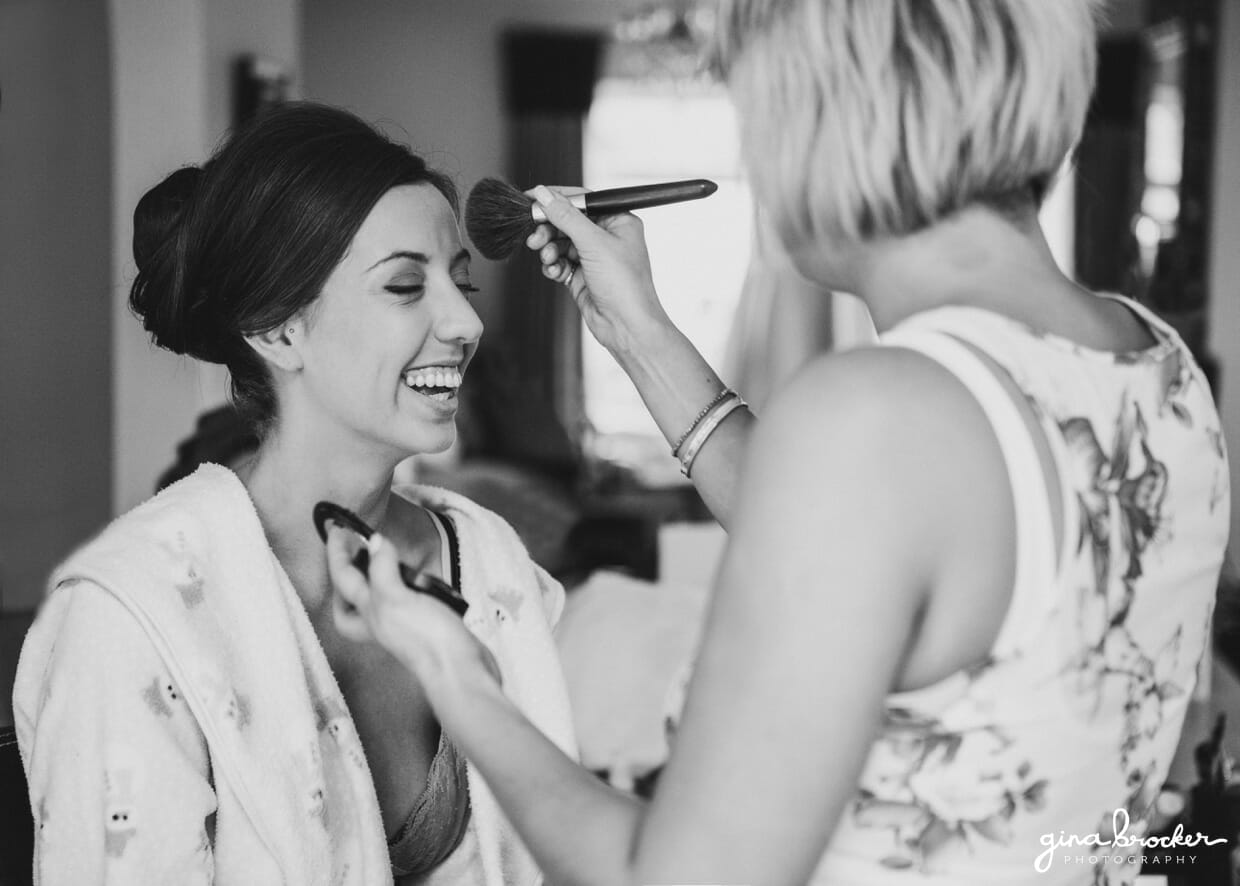 A bride laughs as she gets her makeup done on the morning of her Boston wedding