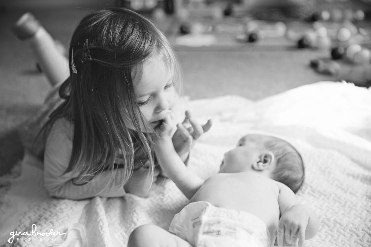 A little girl lays on a blanket with her new baby sister during their Boston family session at home