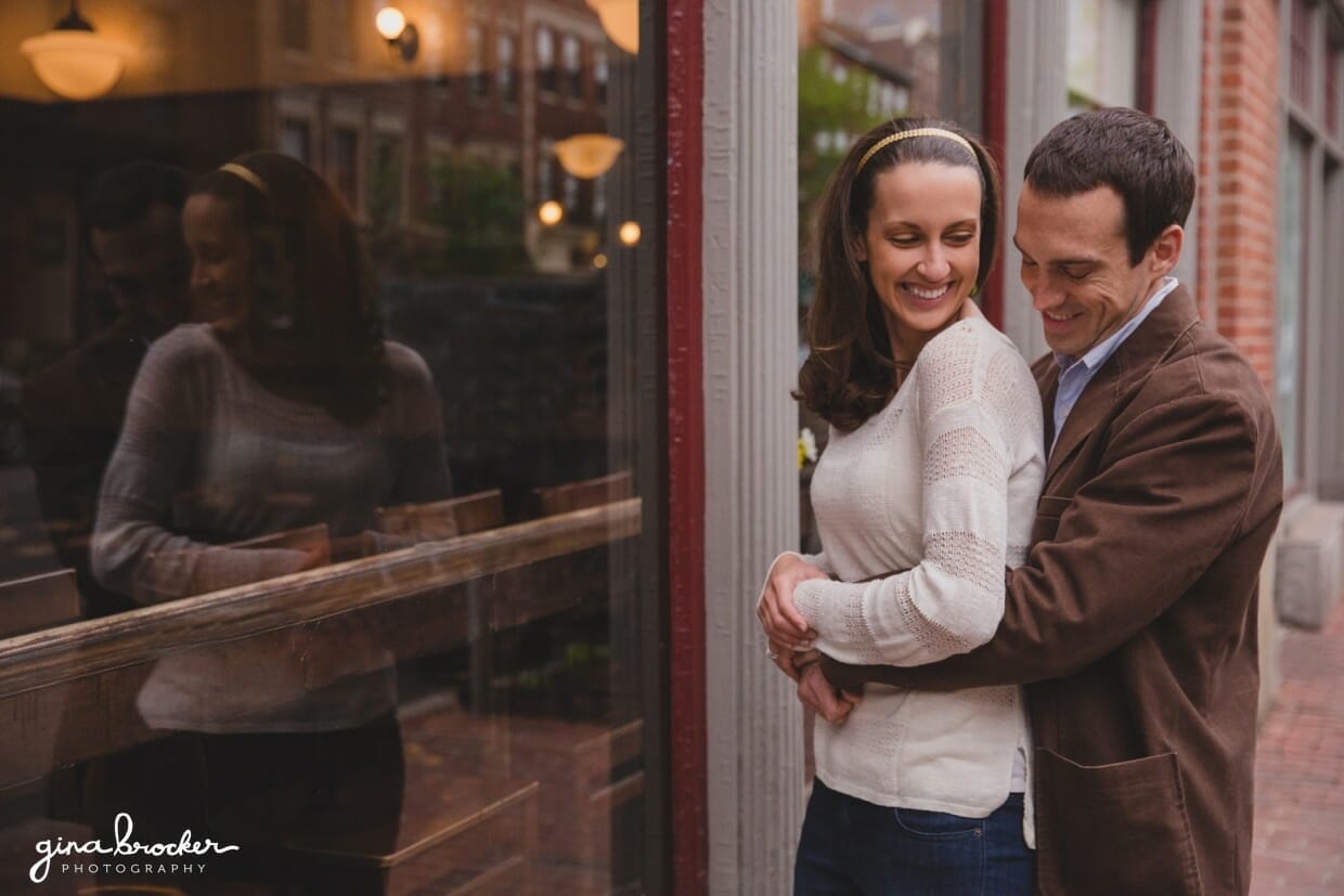 A couple cuddle and laugh outside Panicificio Cafe in Beacon Hill during their sweet couple session in Boston
