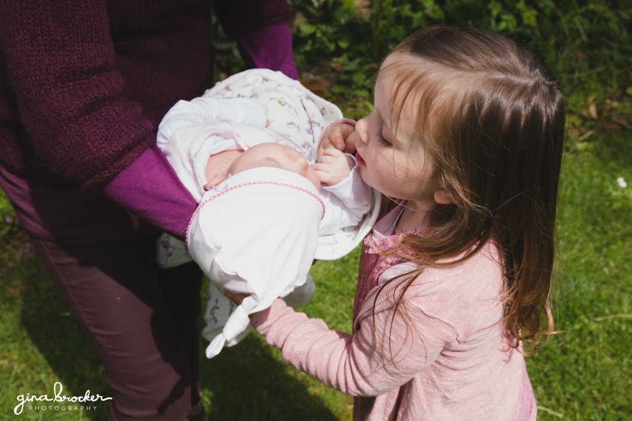 A toddler looks at her baby sister in her mothers arm during a candid family photo session at home