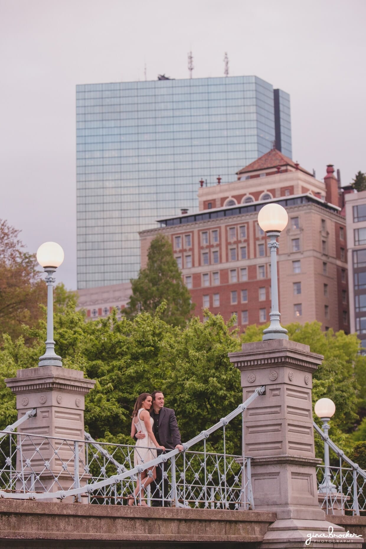 A beautiful portrait of a couple standing on a bridge in the Boston Public Gardens with the Boston skyline in the background