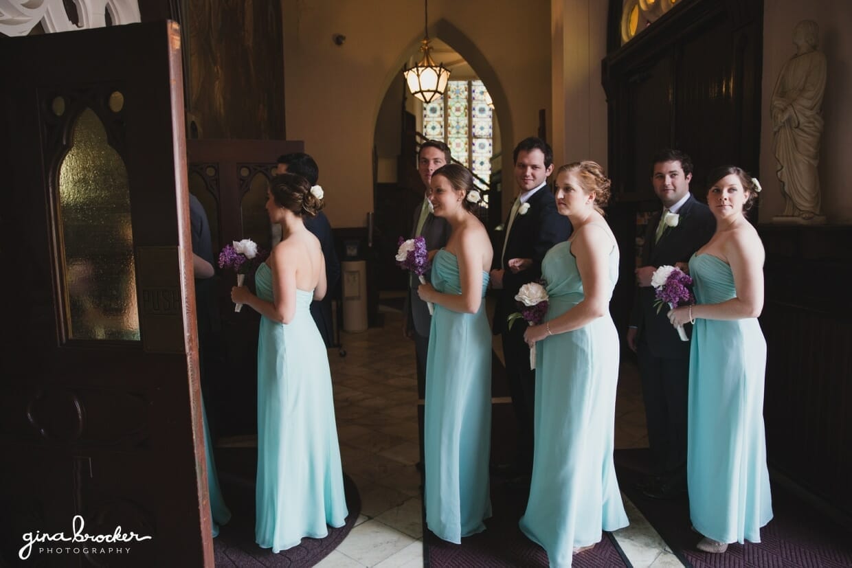 A wedding party wearing aqua gowns and holding lavender bouquets waits to walk up the aisle during a wedding ceremony at the Sacred Heart of Jesus Church in Cambridge, Massachusetts