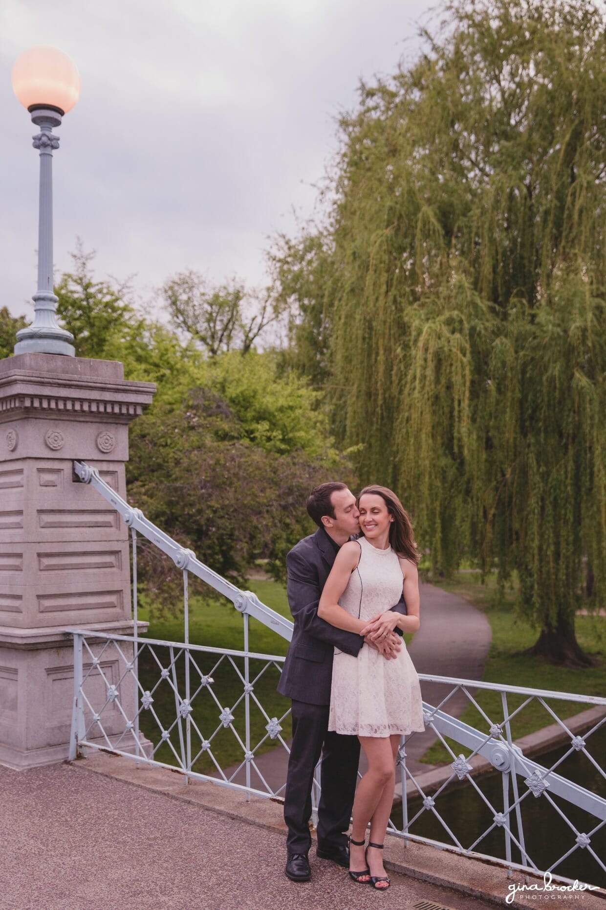 A couple cuddle and kiss on the bridge of the Boston Public Gardens during their sweet engagement session