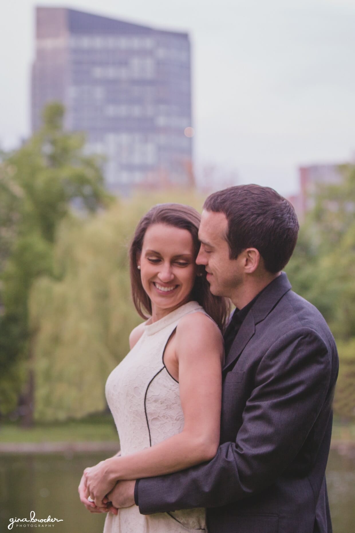 A couple cuddling in the Boston Public Gardens with a view of the back bay during their sweet springtime engagement session
