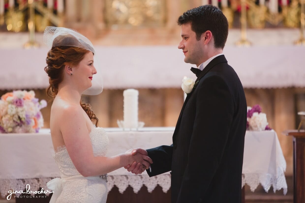 A bride and groom smile at each other as they make their wedding vows in the Sacred Heart of Jesus Church in Cambridge, Massachusetts