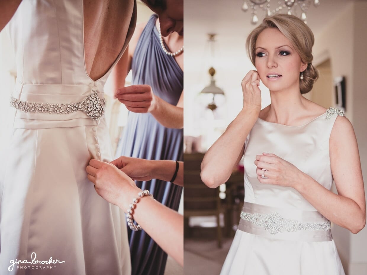The bridesmaids button the brides classic satin wedding gown with silver accents on the morning of her classic garden wedding