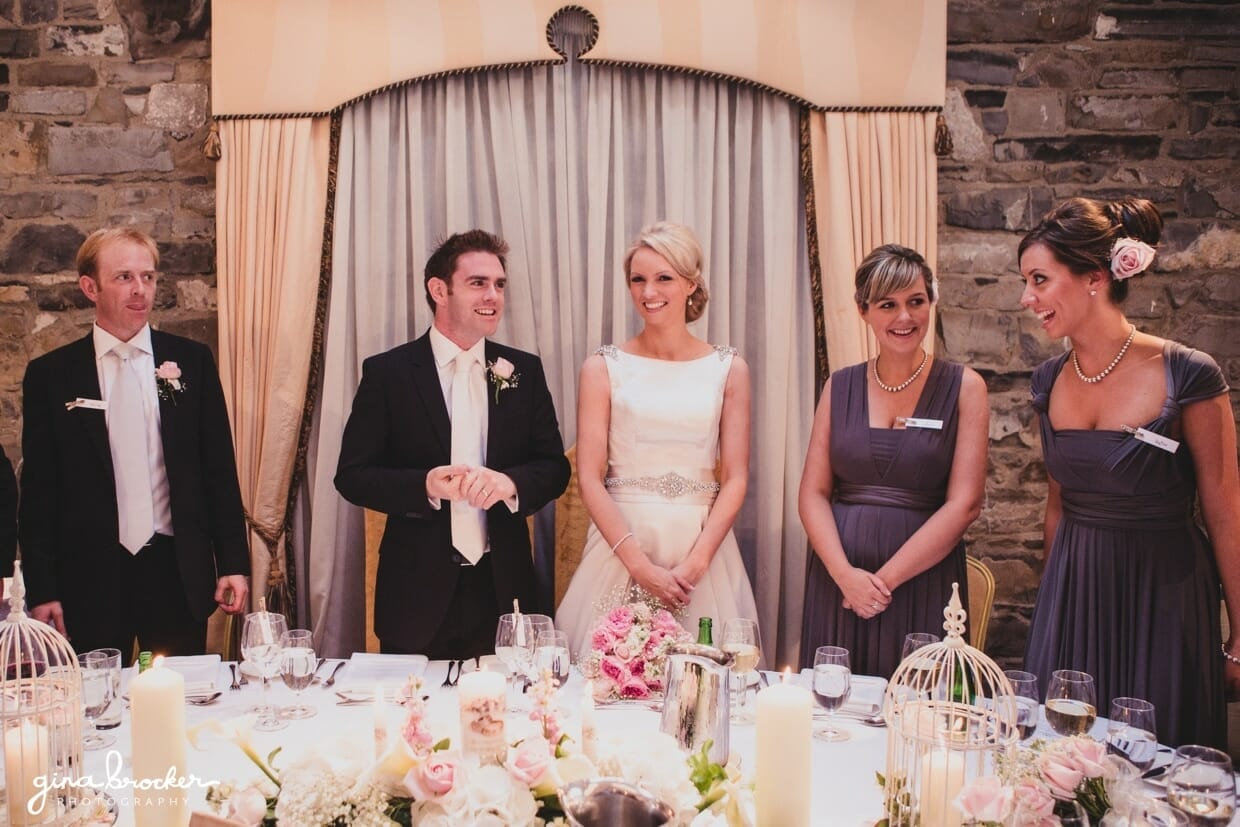 The bride and groom stand with their wedding party at the top table during their wedding reception welcome toast