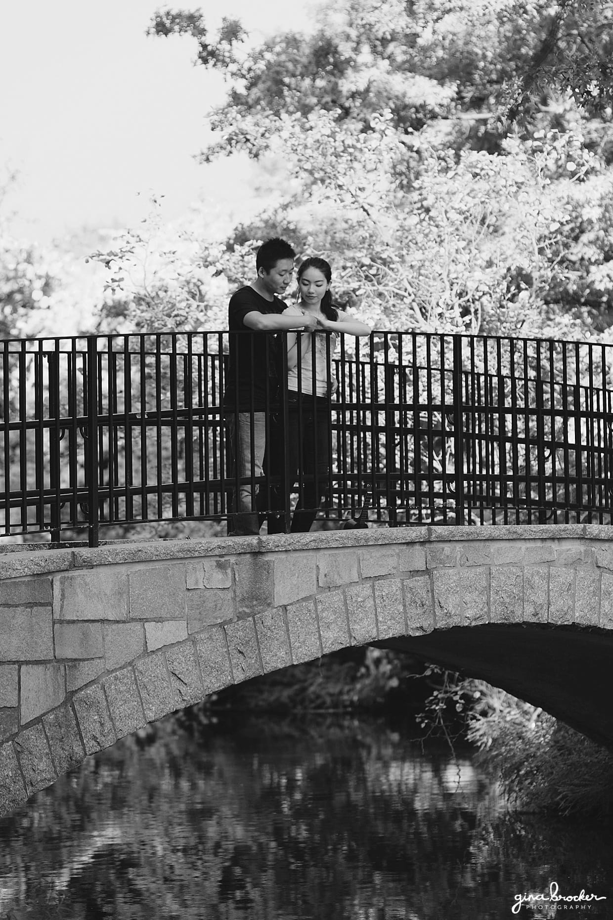 A couple stand together on a bridge during their boston engagement session in back bay fens park. 