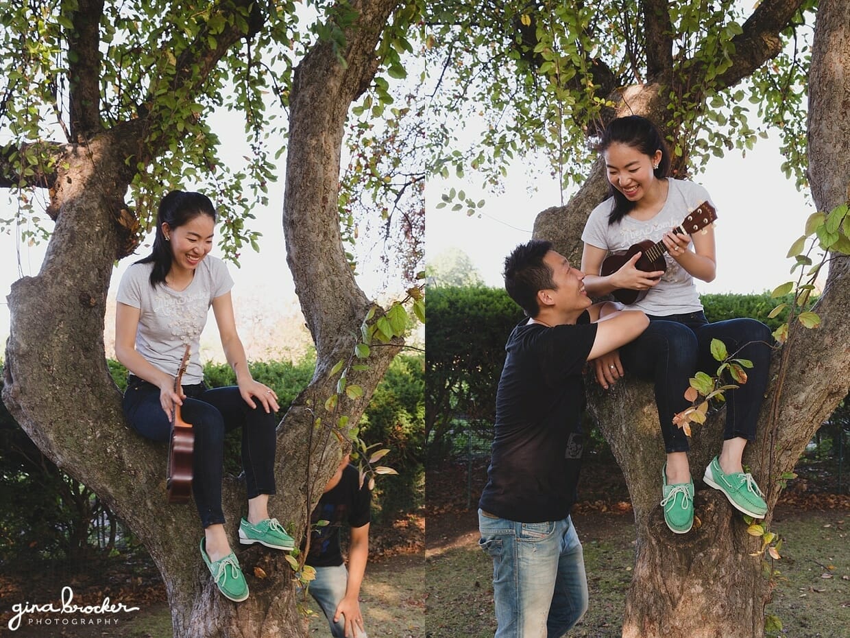 A couple laugh and play music by a tree during their park engagement session in Boston's Back Bay Fens