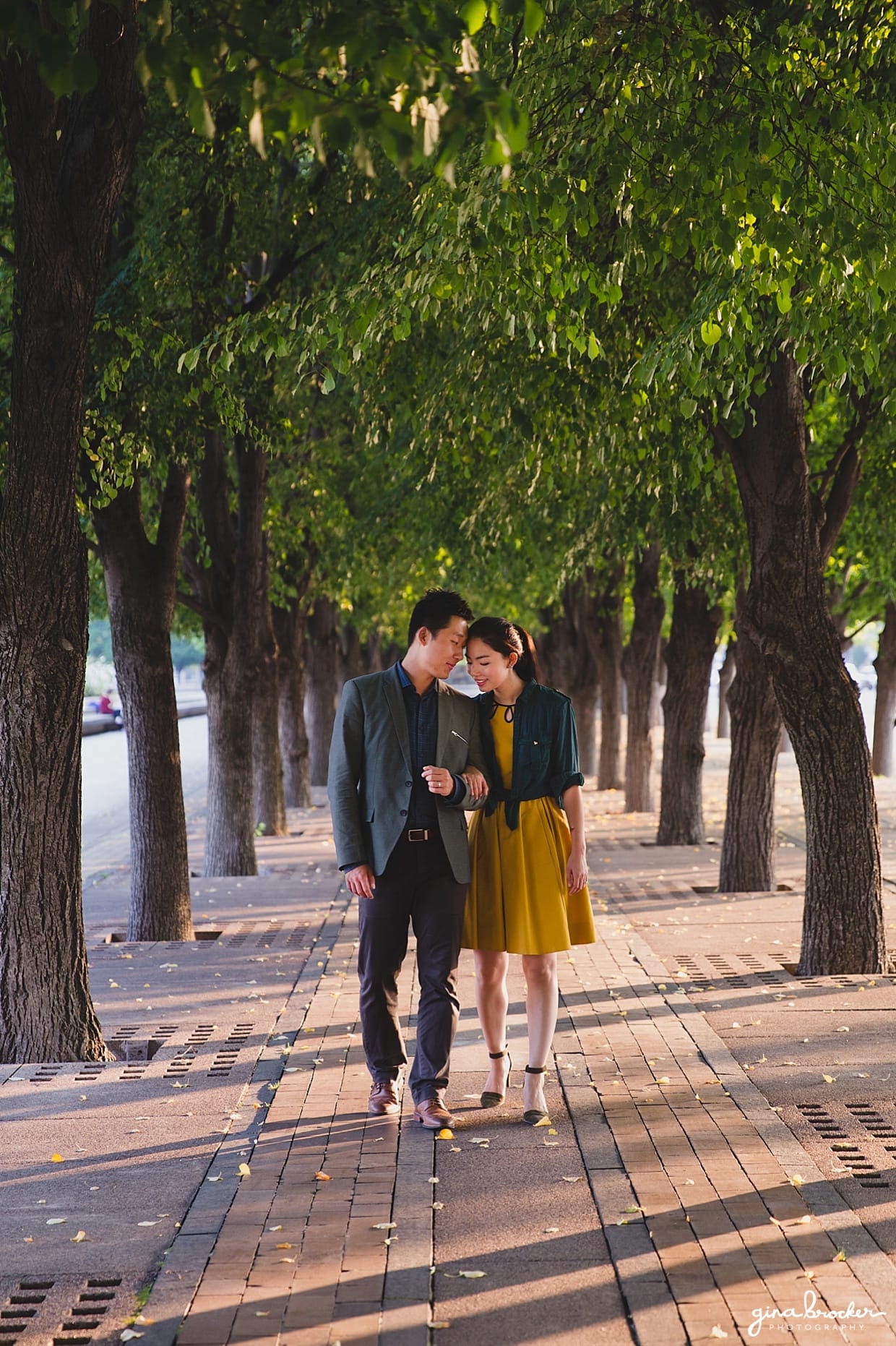 A couple walk arm and arm through a tree lined path just outside the Christian Science Center during their Boston Engagement Session