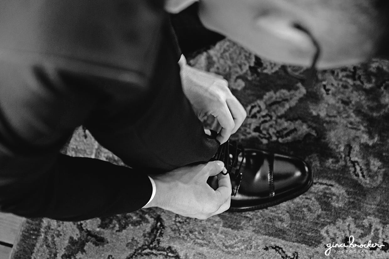 An artistic photograph of the groom tying his shoes on the morning of his hammond castle wedding in gloucester, Massachusetts