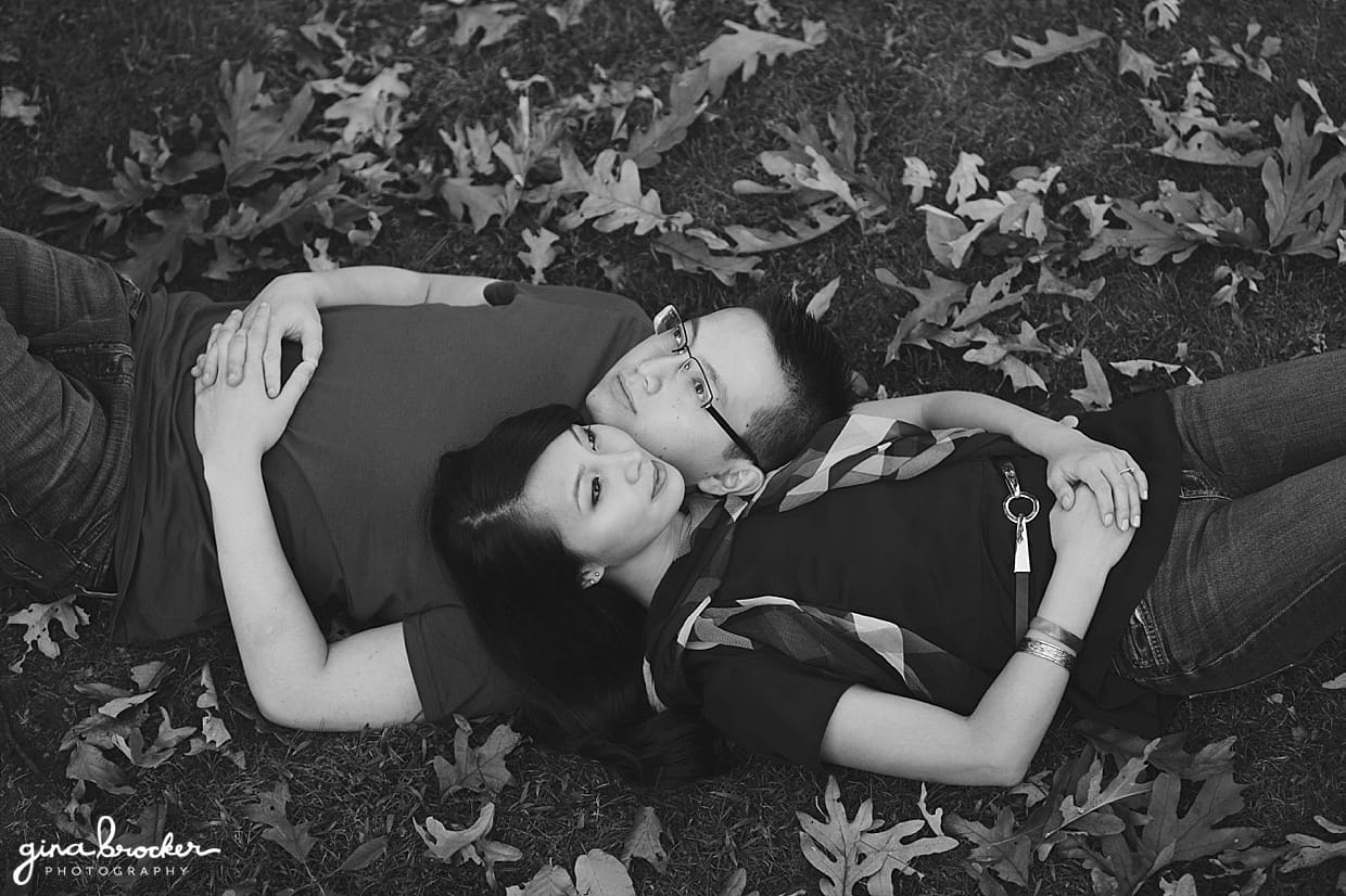 A couple lay on the grass and fallen leaves during their fall engagement session in Newton, Massachusetts