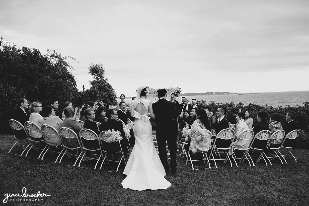 A father walks his daughter up the aisle during an outdoor wedding ceremony in Hammond Castle