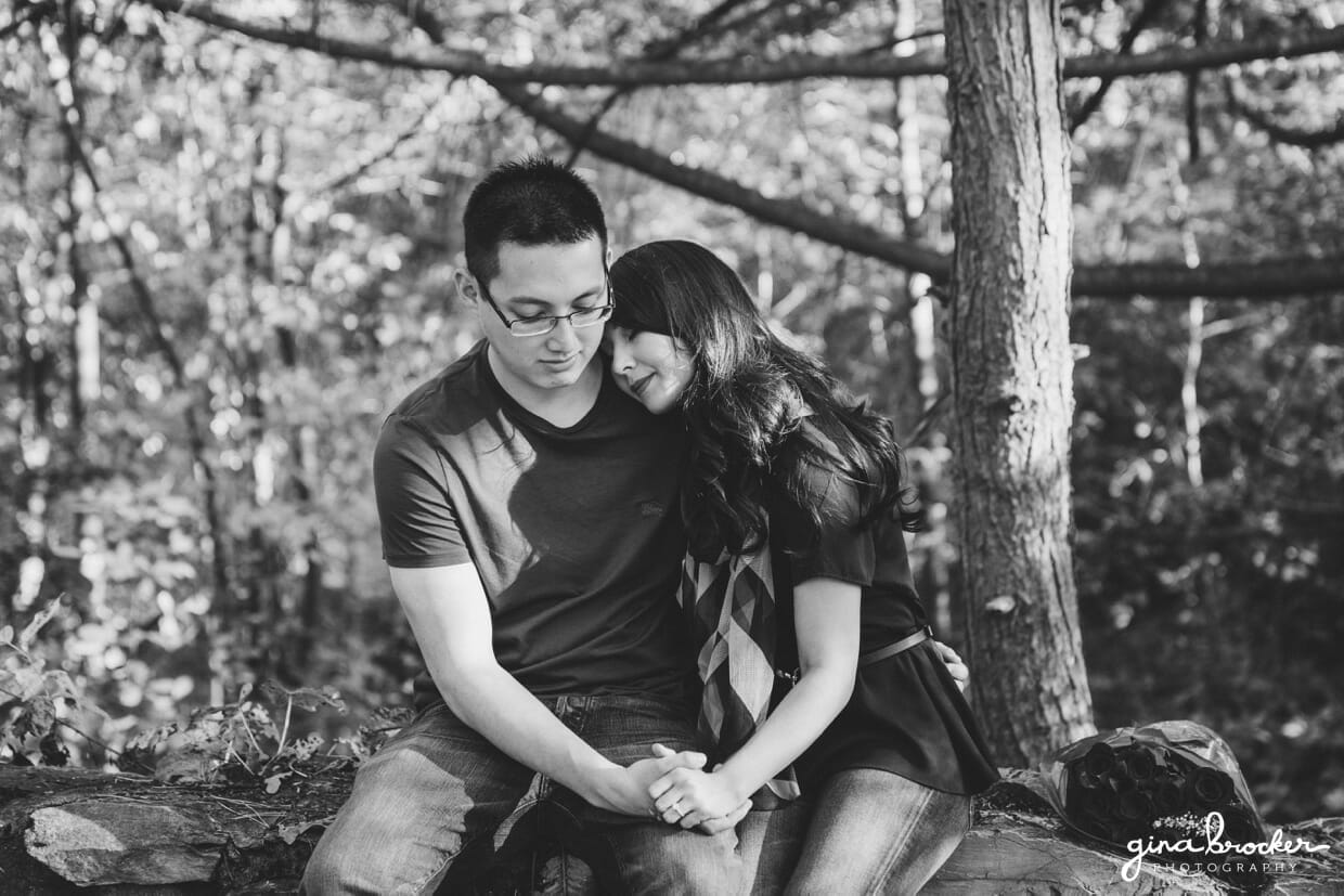 A couple sit on a bridge in the woods during their fall themed boston engagement session