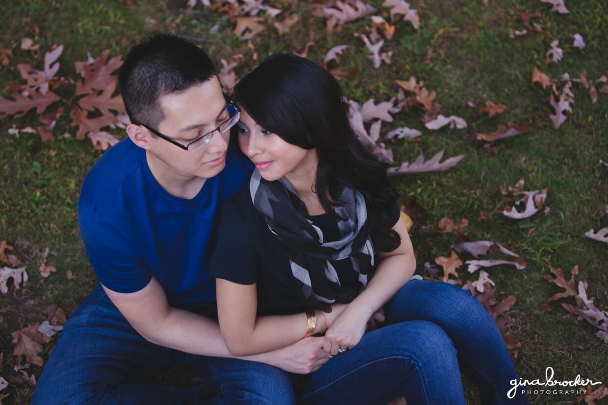 A couple sit together on fallen leaves during their fall engagement session in boston