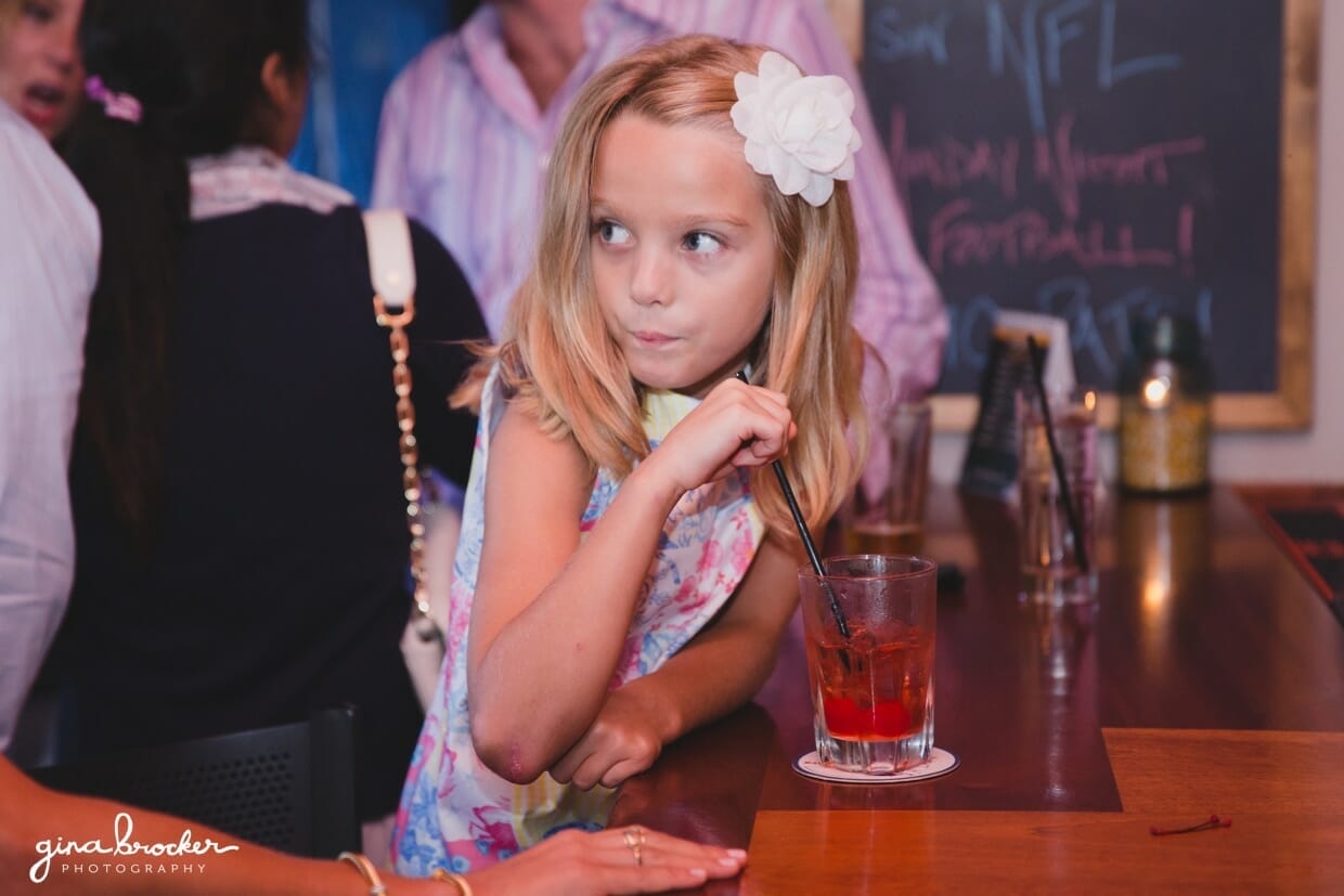 A candid portrait of a little girl taking a sip from her drink during a wedding rehearsal dinner at Backyard BBQ restaurant in Nantucket, Massachusetts
