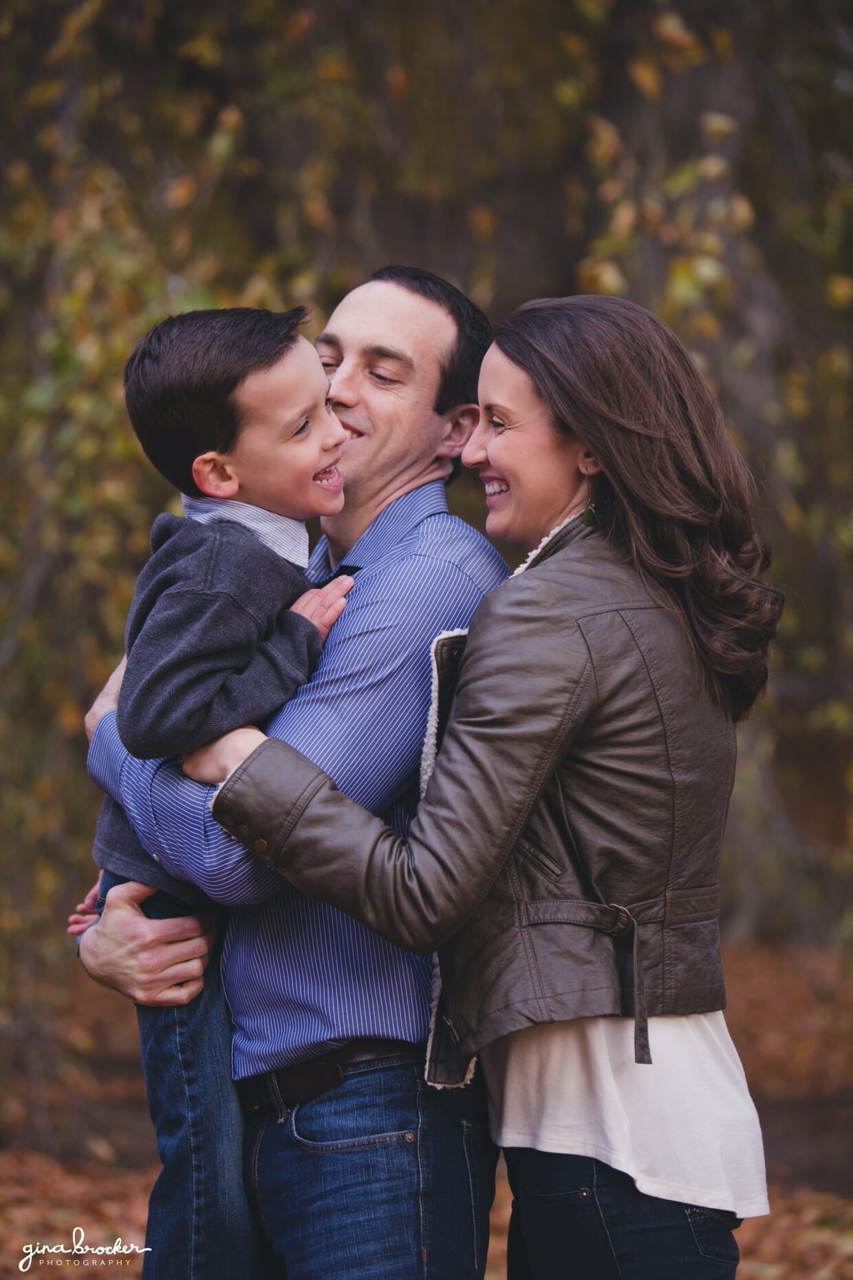 A mom and dad hold and tickle their son during a fall family photo session at the Arnold Arboretum in Boston, Massachusetts