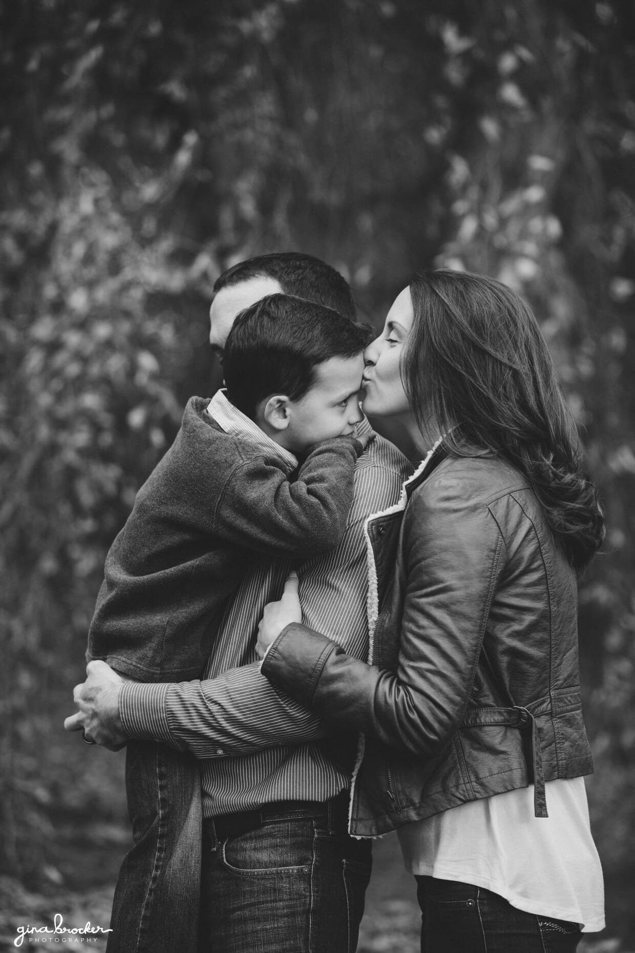 A mother kisses her sons forehead during their natural photo session in Boston's Arnold Arboretum