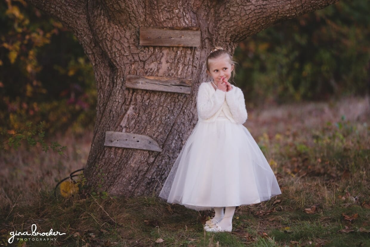 A cute portrait of a flower girl standing by a tree during a farm wedding in Oxford, Massachusetts