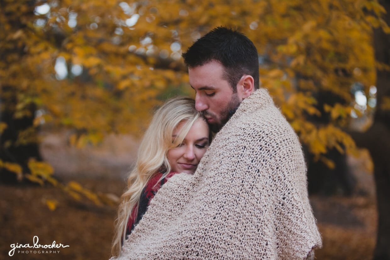A couple snuggle together under a blanket during their fall couple session at the Arnold Arboretum in Boston, Massachusetts