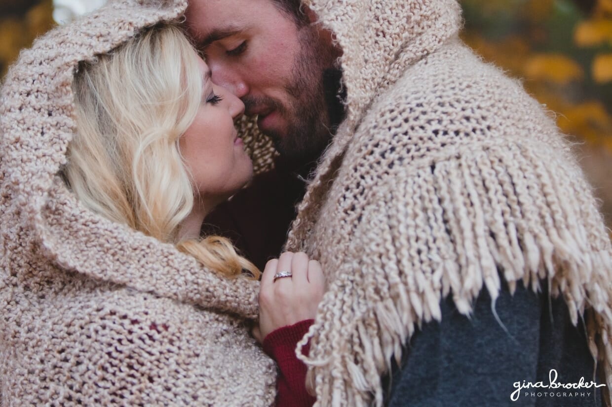 A couple share a kiss under a blanket during their fall couple session in Boston's Arnold Arboretum