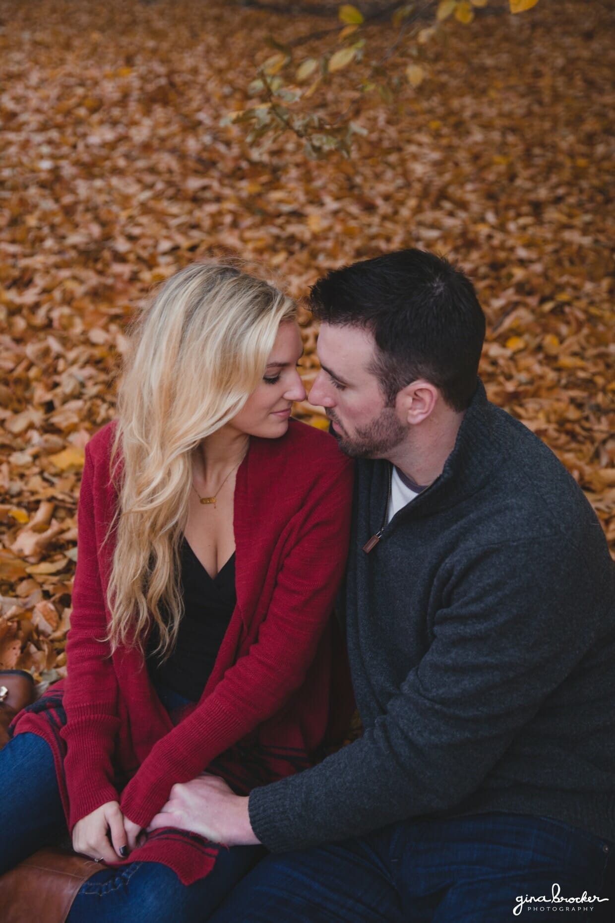 A couple sit together on a blanket during their fall couple session at the Arnold Arboretum in Boston, Massachusetts