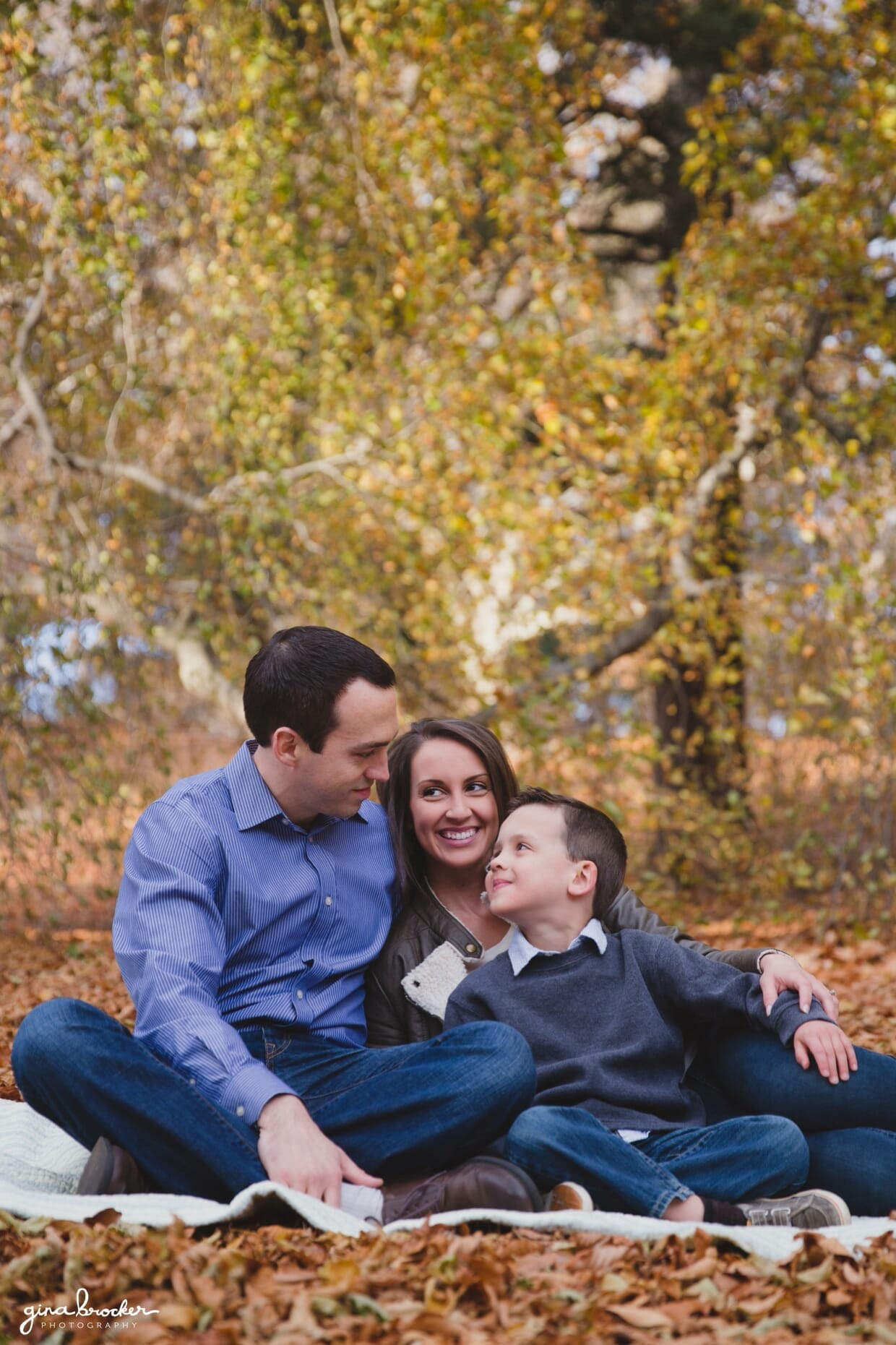A family sit together on a blanket during their fall family photo session at the Arnold Arboretum in Boston, Massachusetts