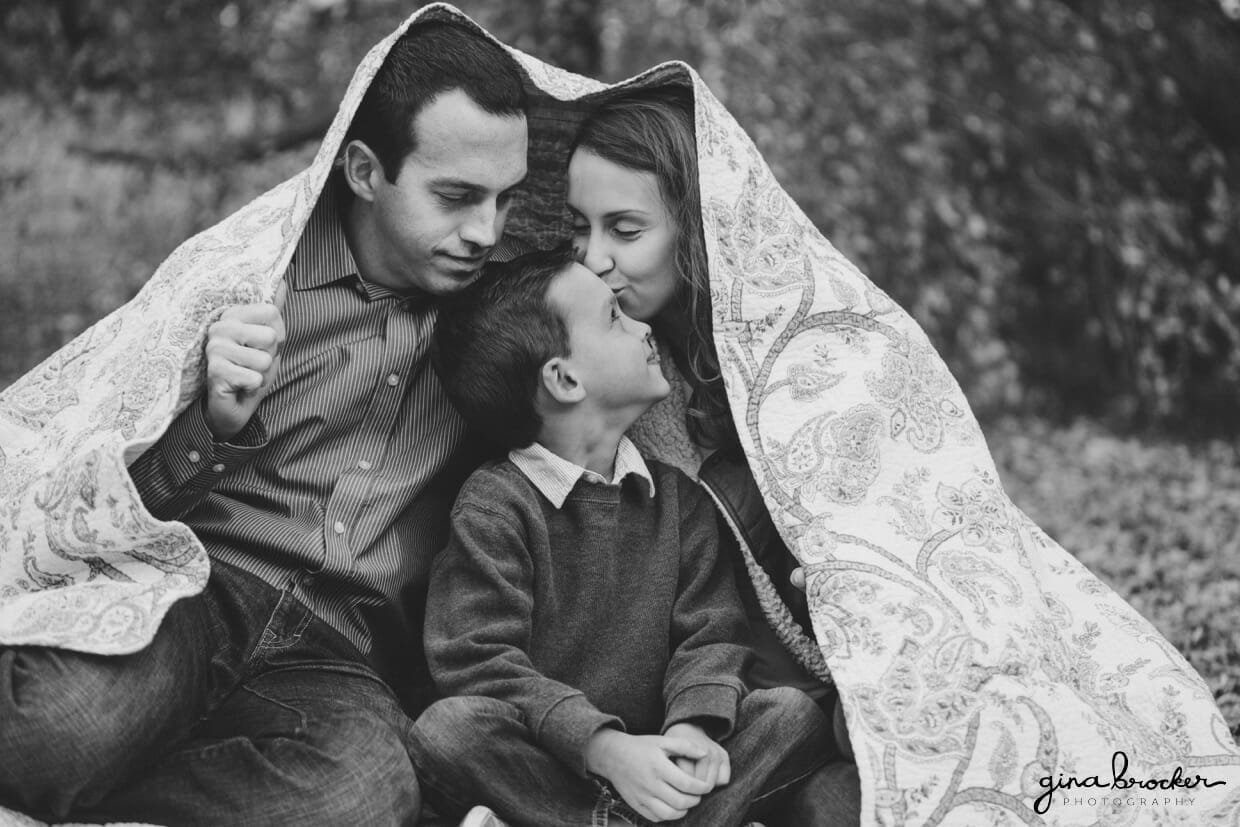 A family cuddle into a blanket during their fall family photo session in Boston's Arnold Aboretum